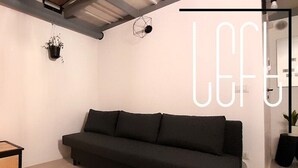 Ein modernes Wohnzimmer mit einer schwarzen Couch, einem kleinen Rollwagen und einer hängenden Pflanze.