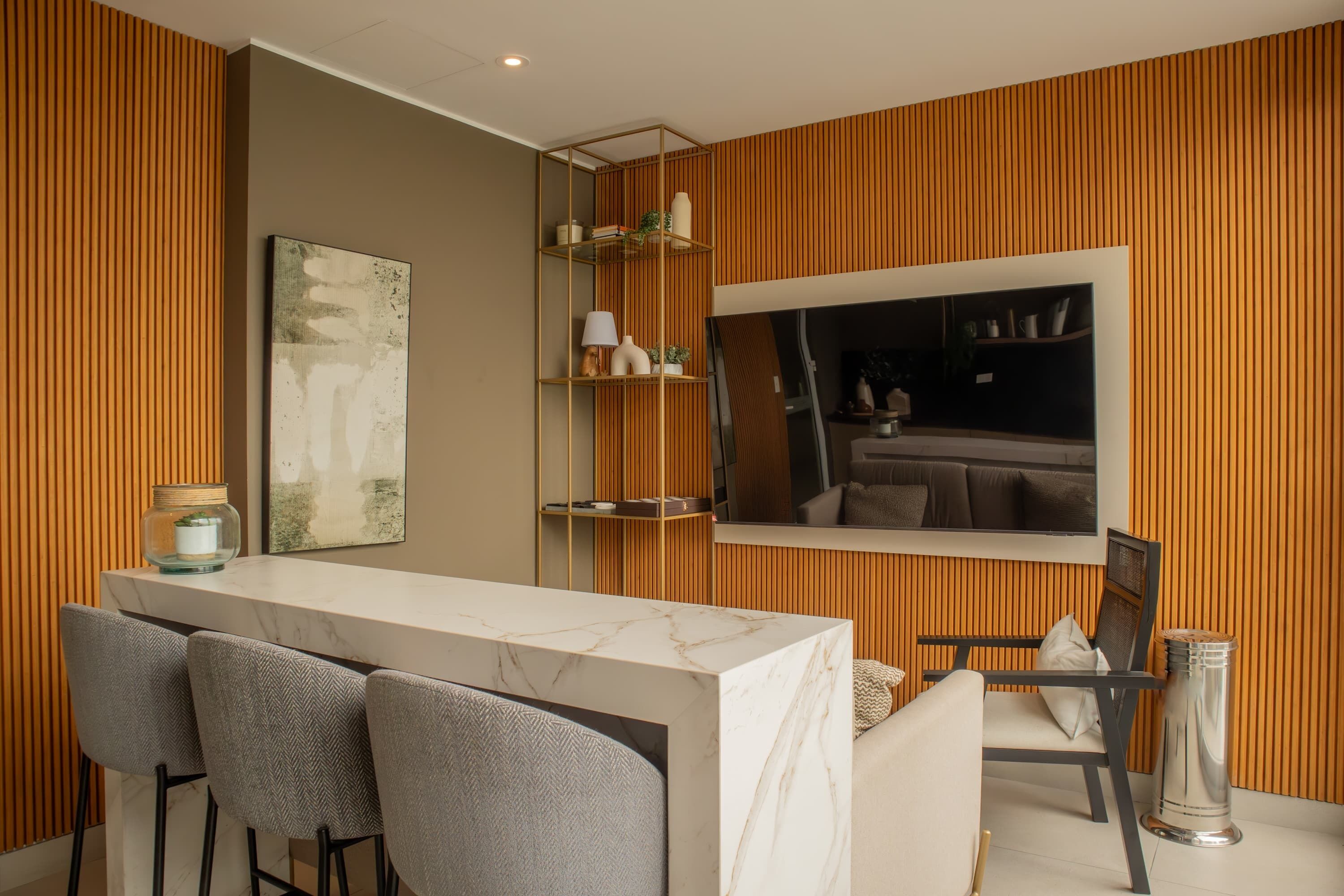 Een moderne eethoek met een marmeren aanrecht, grijs beklede stoelen, een grote spiegel en houten lambrisering.