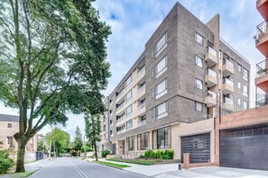 A modern multi-story residential building with balconies, large windows, and a well-maintained lawn.