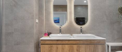 A modern bathroom with two oval mirrors, wooden vanity, and a shower area.
