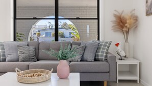 Uma sala de estar moderna com um sofá cinzento, uma mesa de centro branca, um vaso rosa e uma pequena mesa lateral branca com um pássaro decorativo e capim-do-campo.