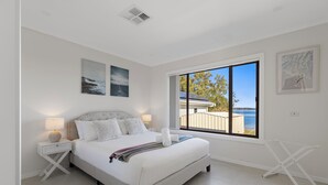 Quarto com uma cama grande, mesa de cabeceira com abajur, janela com vista para o mar e um respiradouro no teto.