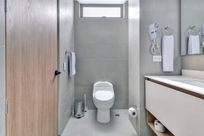 Une petite salle de bain équipée de toilettes, d’un sèche-mains, d’un porte-serviettes et d’un miroir.