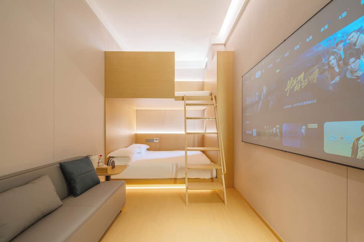 Ein modernes Hotelzimmer mit Etagenbett, einer Schlafcouch, einer Himmellaune und einem großen Bildschirm, der Filme zeigt.