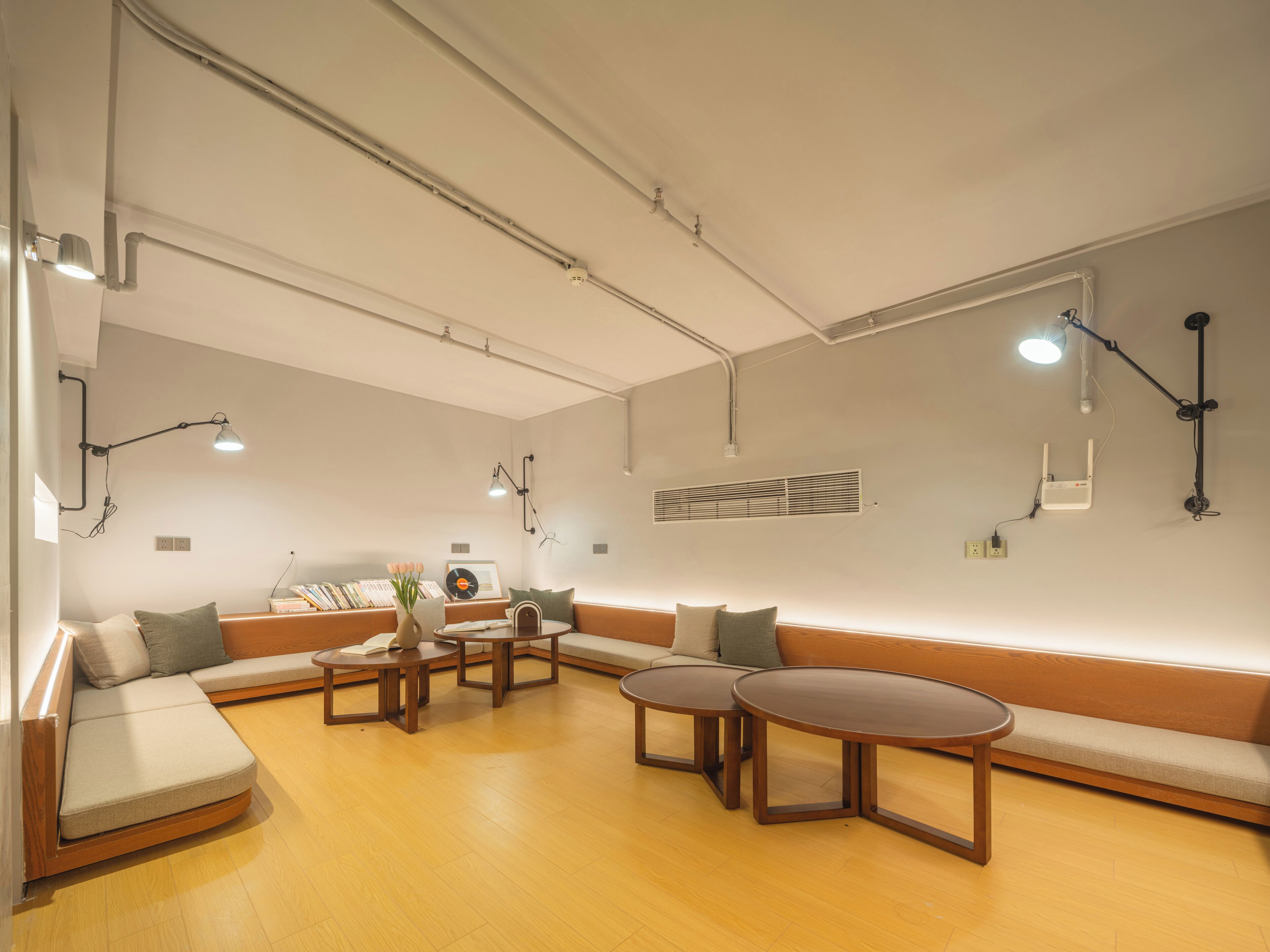 Una sala moderna con un sofá seccional, dos mesas redondas y un equipo de aire acondicionado de pared.