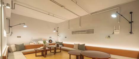 Una sala moderna con un sofá seccional, dos mesas redondas y un equipo de aire acondicionado de pared.
