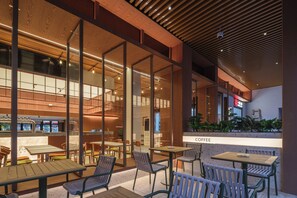 Un café moderne avec des tables et des chaises en bois, de grandes fenêtres et un panneau indiquant l’emplacement du coin café.