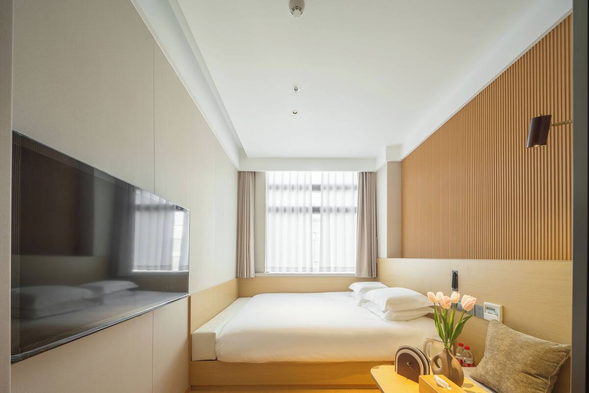 Ein Hotelzimmer mit Bett, Fernseher, einer Wand aus Holzpaneelen und einem Fenster mit Vorhängen.