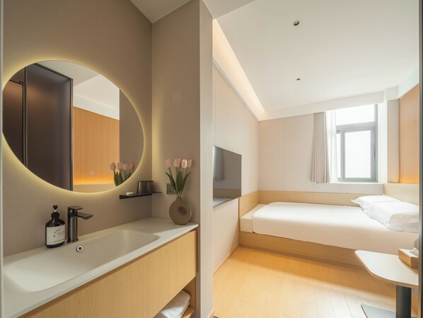 A modern hotel room with a large mirror, a bedside table, a bed, and a window with curtains.