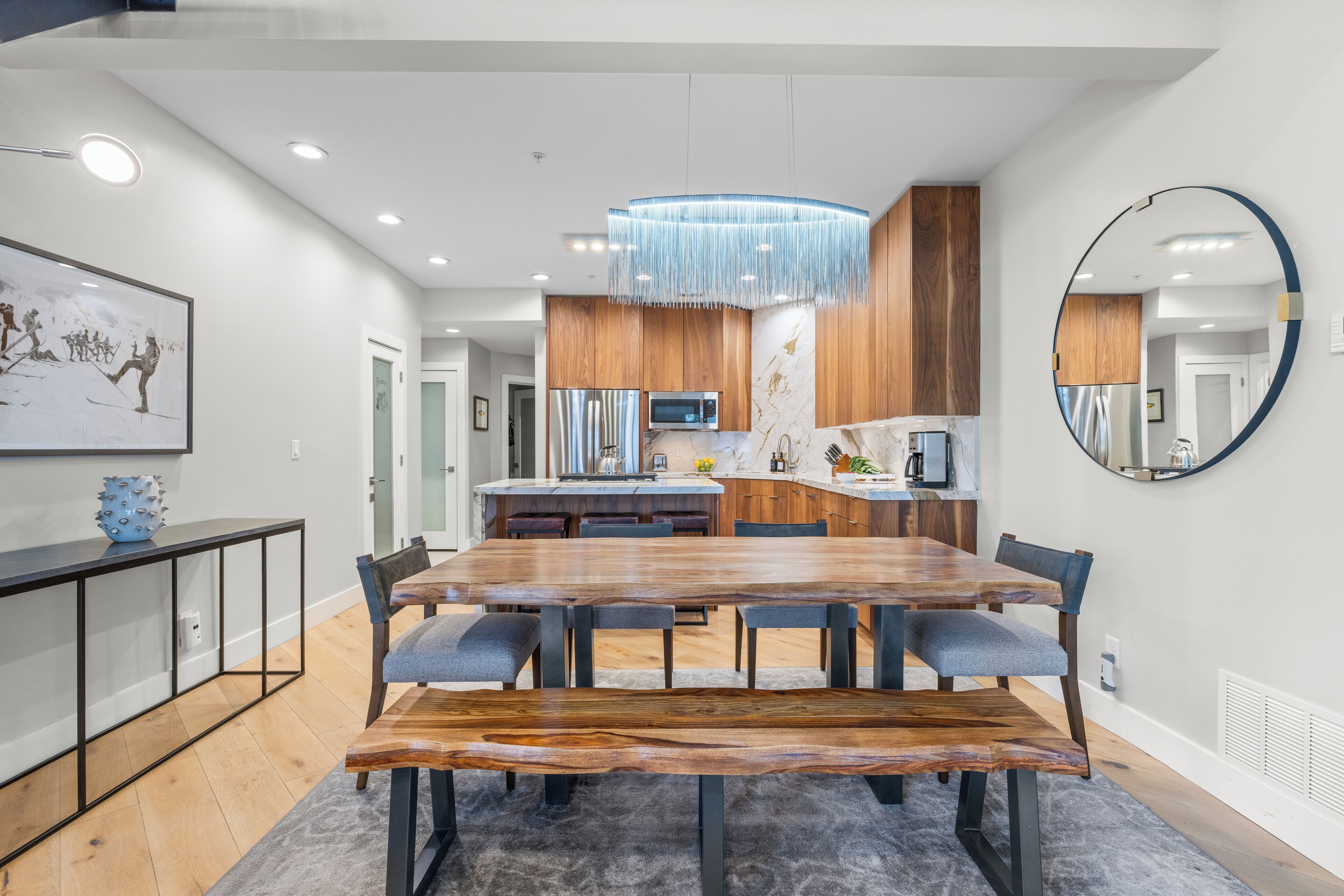 Un espace repas moderne avec une table et des chaises en bois, un lustre et un grand miroir au mur.