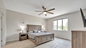 Ein Schlafzimmer mit einem hölzernen Bett, einem Deckenventilator, Nachttischen mit Lampen und einem großen Fenster.