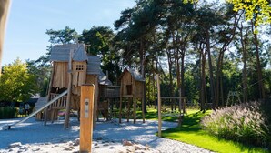 A wooden play structure with slides and climbing areas, surrounded by trees and a grassy area. - Peaceful Stay Near Trails (Veldhoven)