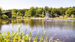 A lakeside view with a fountain, surrounded by cabins and lush greenery. - Peaceful Stay Near Trails (Veldhoven)