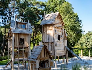 Houten speeltuintjes met ladders en glijbanen, omgeven door bomen.