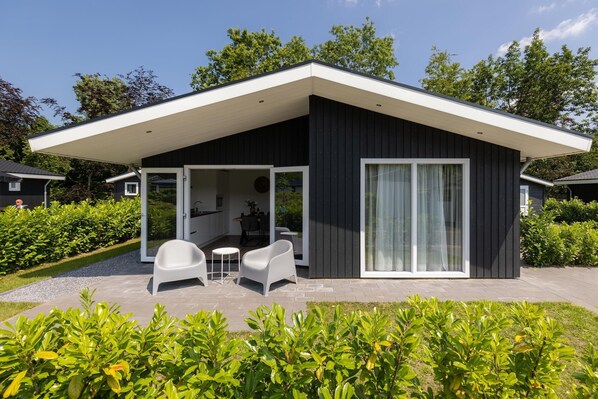 A modern house with a covered patio, white chairs, and a dining table. - Peaceful Stay Near Trails (Veldhoven)