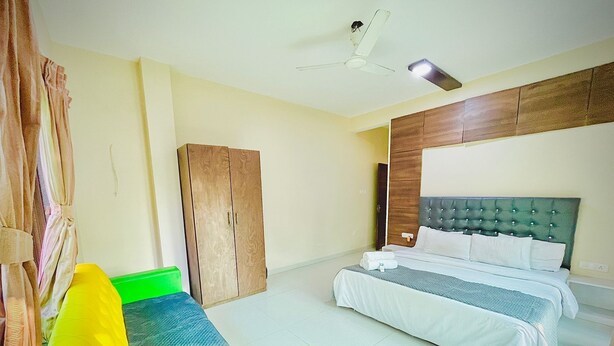 A hotel room with a bed, a wardrobe, a green sofa, and a ceiling fan. - Hotel Saiom Palace (Raipur)