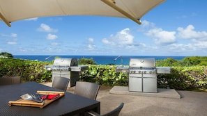 En utomhusplats för måltider med två grillar, ett bord med bestick och utsikt över havet.