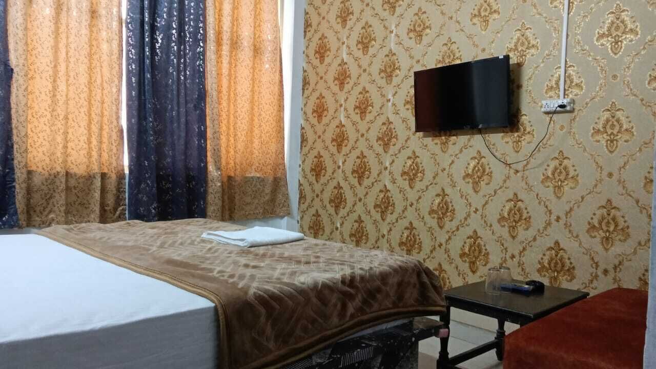 Ένα δωμάτιο ξενοδοχείου με ένα κρεβάτι, μια τηλεόραση τοποθετημένη στον τοίχο, ένα μικρό τραπέζι και μια κόκκινη καρέκλα.