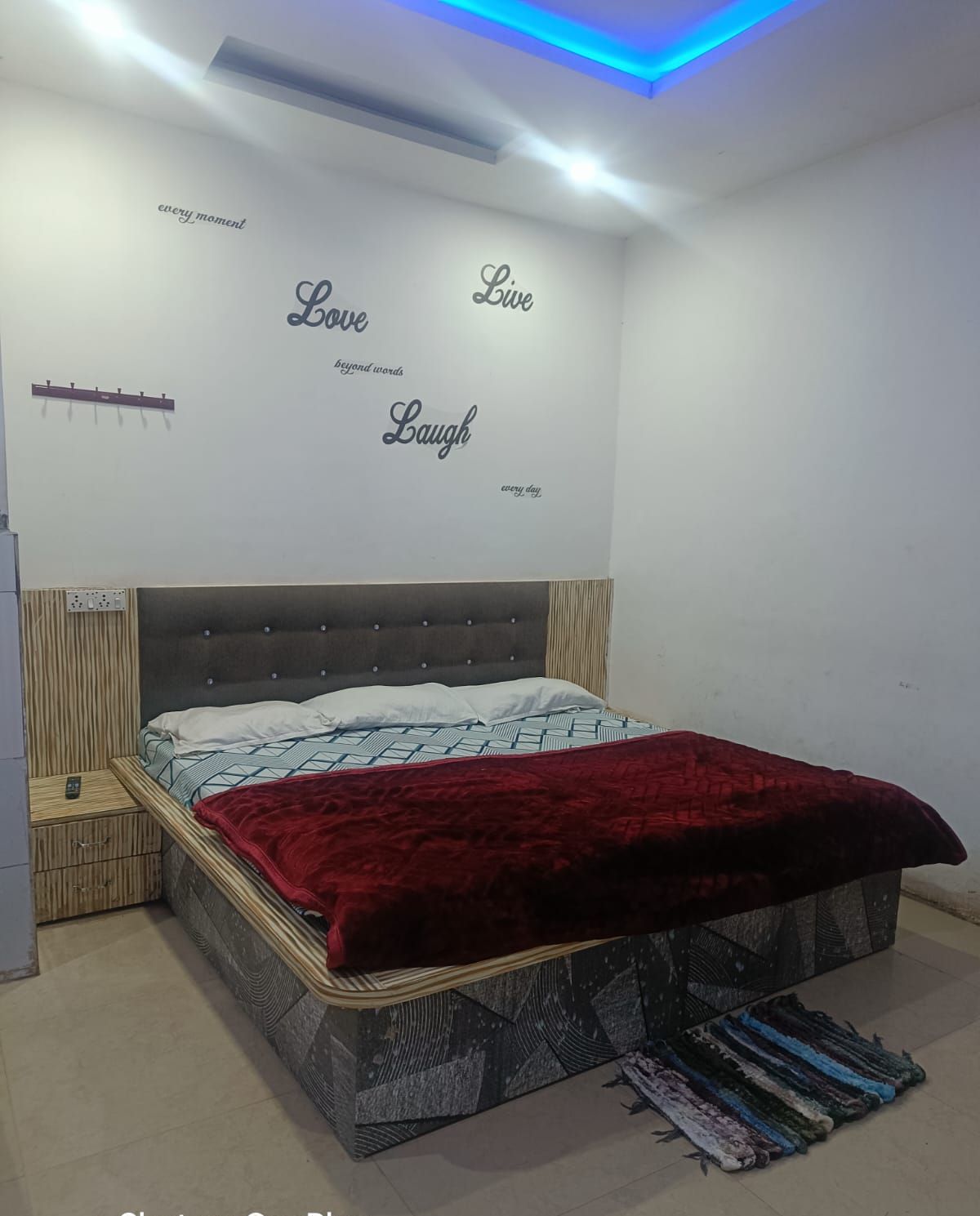 Ein Schlafzimmer mit einem Bett, einem Nachttisch, einer Wand mit motivierenden Zitaten und einer blau beleuchteten Decke.