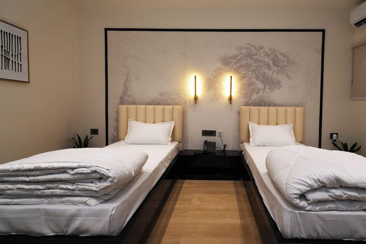 A hotel room with two single beds, a large abstract painting on the wall, and a small table between the beds.