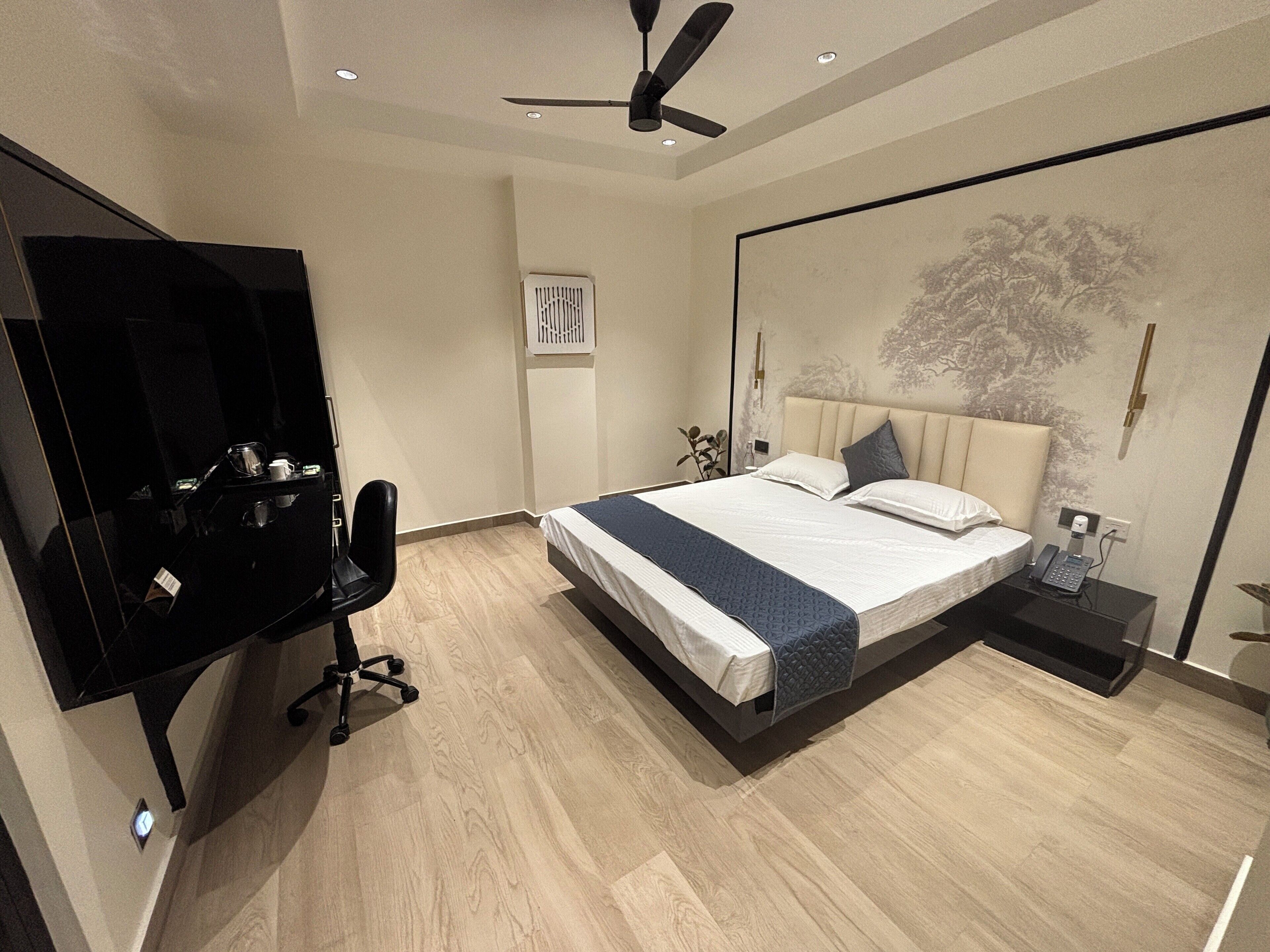 Quarto moderno com cama, escrivaninha, cadeira, ventoinha no teto e ar condicionado fixado na parede.