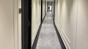 A long, narrow hallway with white walls and black-framed doors. The floor is a polished marble with black borders. - Hotel Kuber (Guwahati)