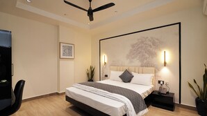 A modern bedroom with a large bed, a ceiling fan, a wall-mounted light, and a framed artwork. - Hotel Kuber (Guwahati)