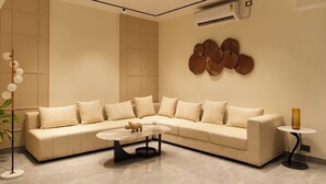 A modern living room with a beige sectional sofa, a round coffee table, and a decorative wall piece. - Hotel Kuber (Guwahati)