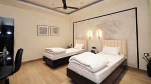 A hotel room with two beds, a desk, and a ceiling fan. - Hotel Kuber (Guwahati)