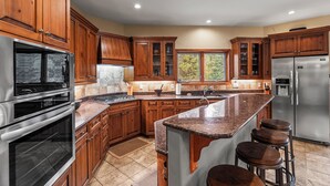 Una cocina moderna con gabinetes de madera, electrodomésticos de acero inoxidable, encimera de granito y un amplio ventanal.