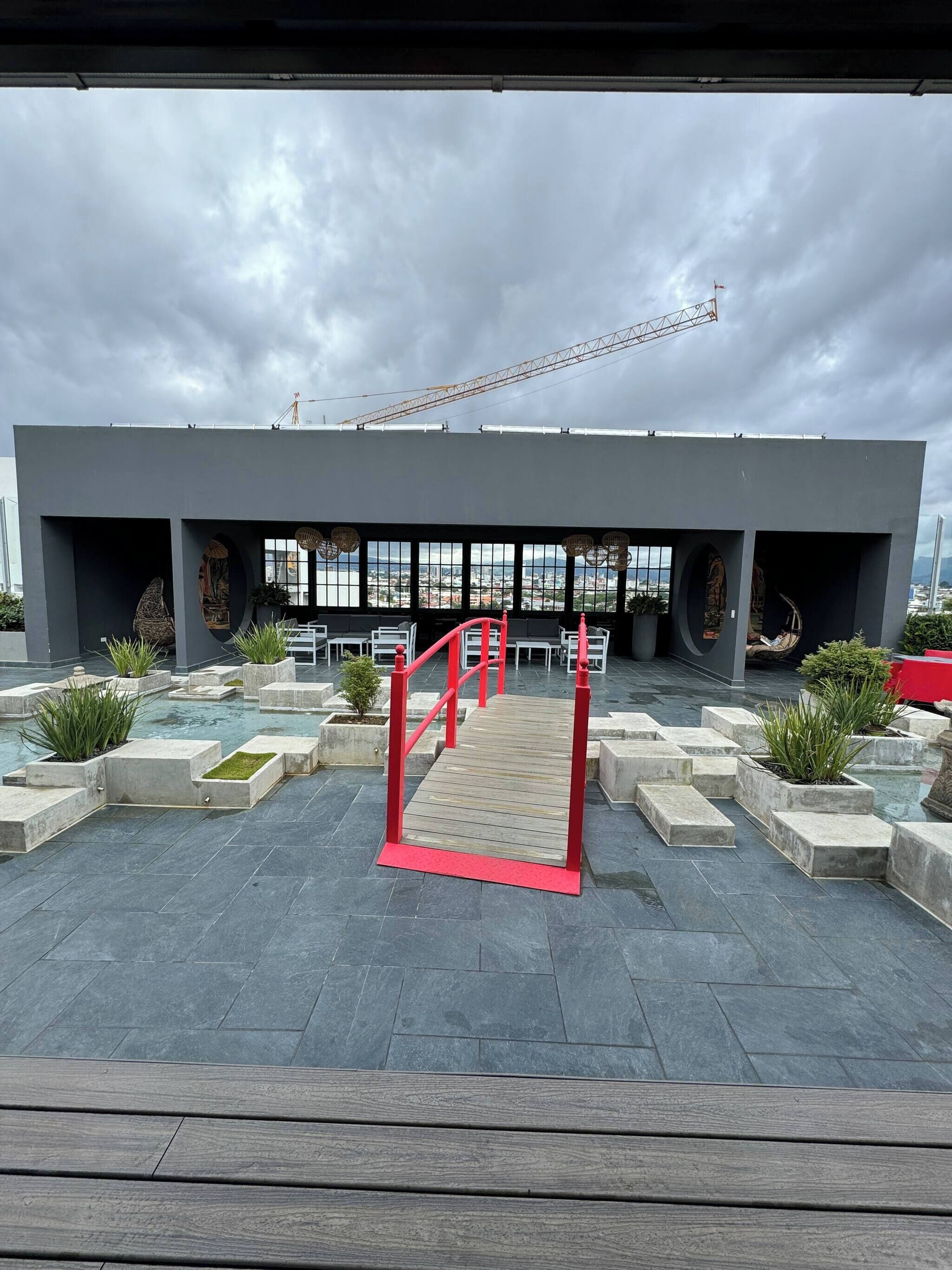 A modern building with a large glass facade, outdoor seating area with red railings, and a view of the cityscape.