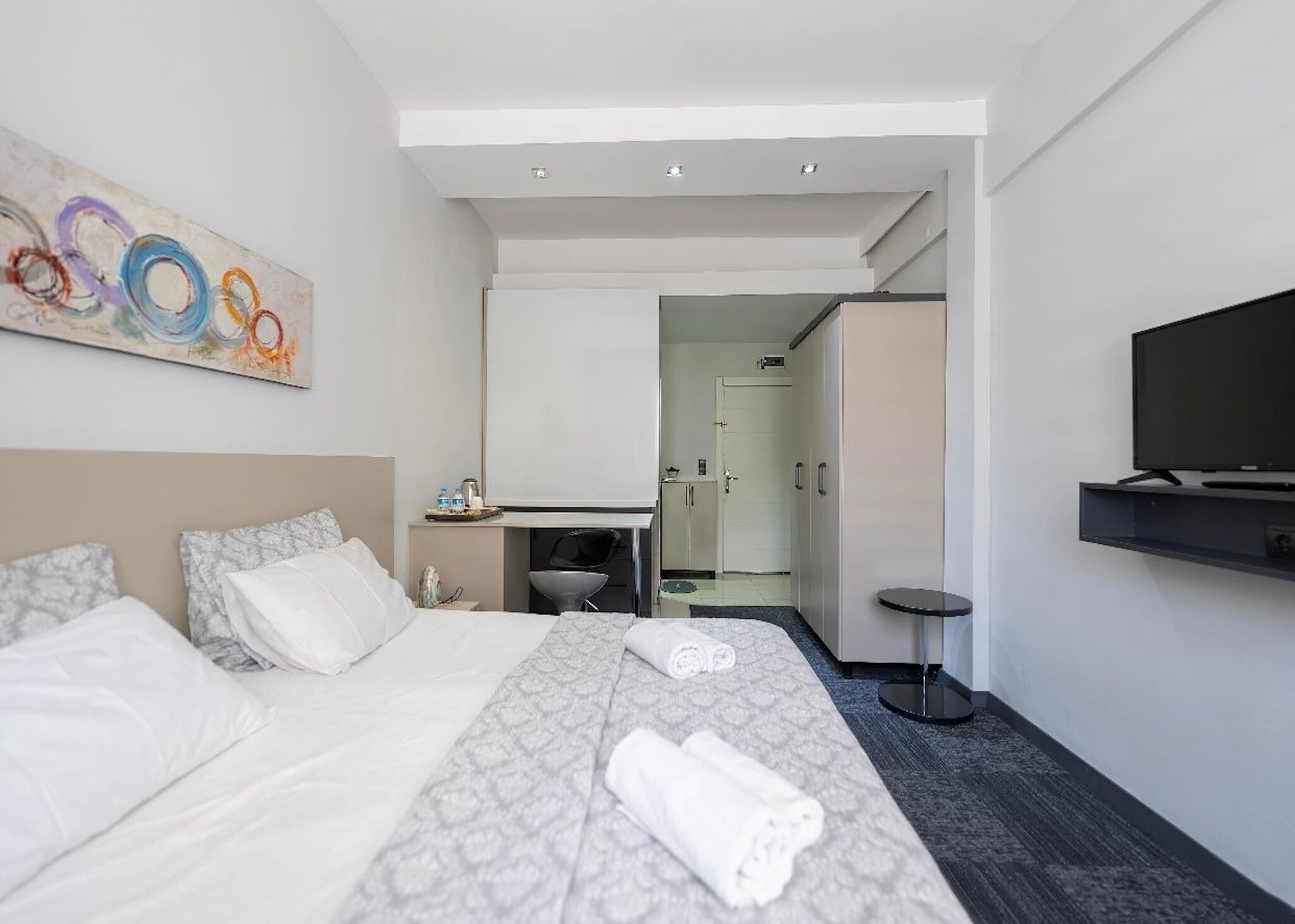 Een hotelkamer met een bed, een bureau, een televisie en een badkamer, zichtbaar door een geopende deur.