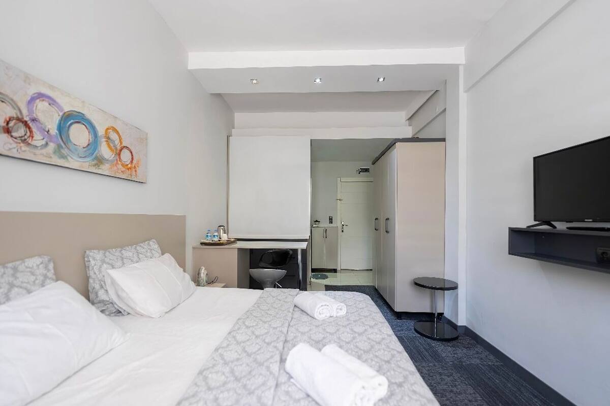 A hotel room with a bed, a desk, a television, and a bathroom visible through an open door.