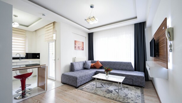 Una sala de estar moderna con un sofá gris, una mesa de centro, una silla roja y una cocina visible a través de una puerta abierta.