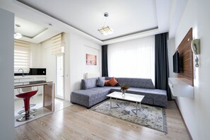 A modern living room with a grey sofa, a coffee table, a red chair, and a kitchen area visible through an open door. - ARGEUS PRESTİJ (Talas)