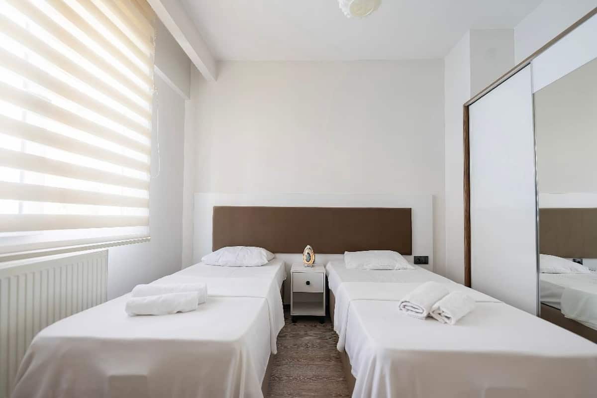 A hotel room with two single beds, a nightstand, a mirror, and a radiator.