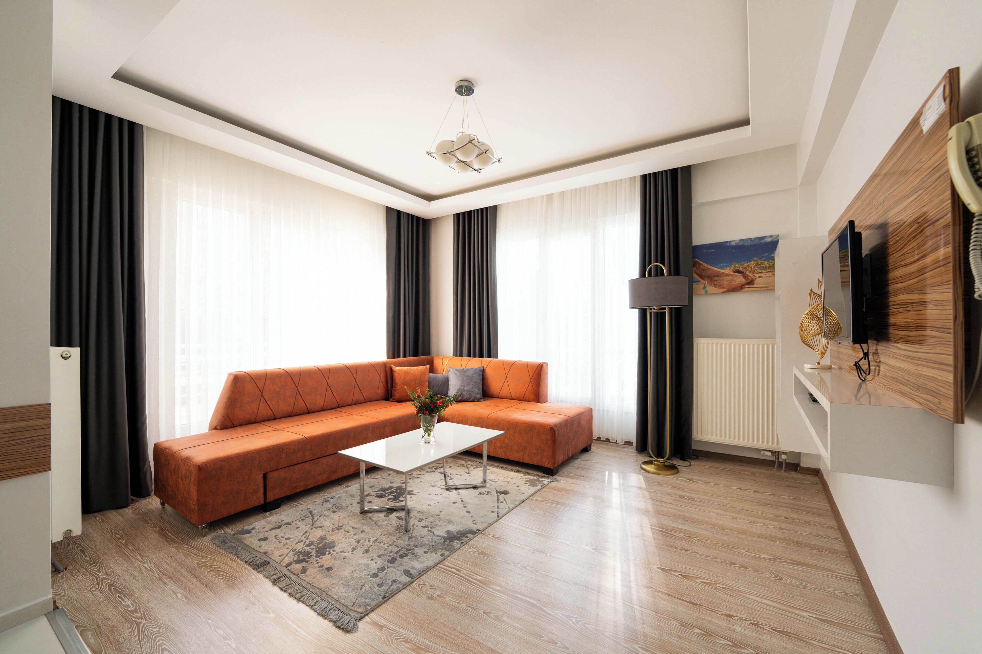 Un salon moderne avec un canapé d’angle, une table basse, un tapis, une suspension et un téléviseur à écran plat fixé au mur.