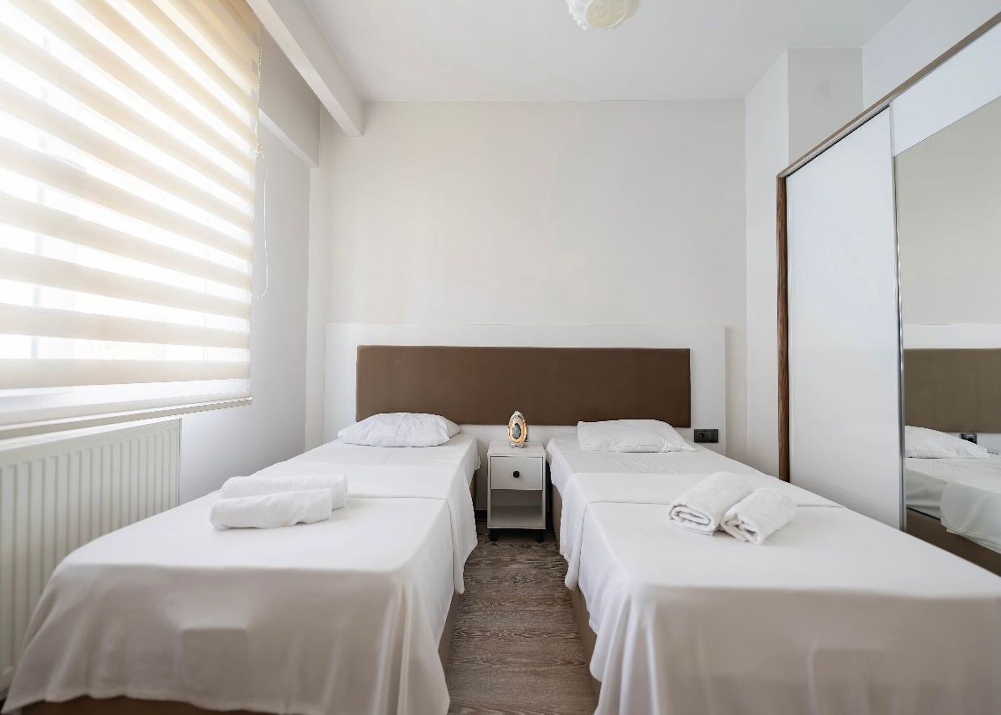 Een hotelkamer met twee eenpersoonsbedden, een nachtkastje, een spiegel en een radiator.