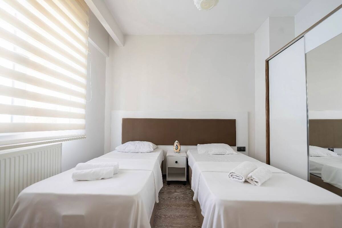 A hotel room with two single beds, a nightstand, a mirror, and a radiator.