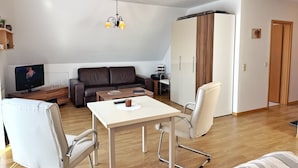 Un salon moderne comprenant un canapé, deux fauteuils, une table basse, un téléviseur et une armoire.