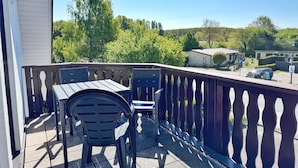 Un balcon avec une table et des chaises, donnant sur un parking et entouré de verdure.