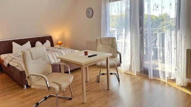 Une chambre d’hôtel moderne, dotée d’un canapé, de deux fauteuils, d’une petite table, d’une lampe et offrant une vue sur la ville grâce à de grandes fenêtres.