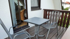 A balcony with a table and two chairs, a wicker chair inside, and a view of a house in the background. - Vacation apartment Baltique 4 (Glowe)