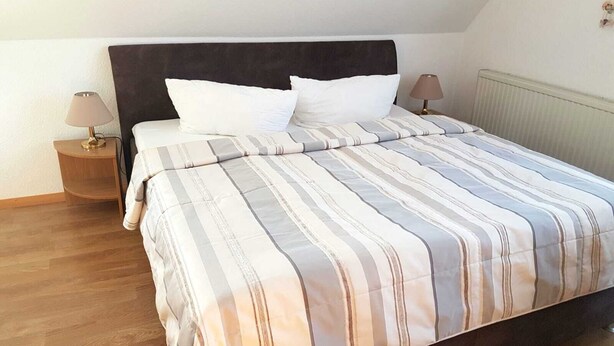 A bedroom with a bed, two bedside tables, a lamp on each table, and a radiator on the wall. - Vacation apartment Baltique 4 (Glowe)