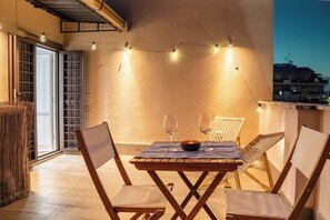 A balcony with a wooden table and chairs, string lights, and a view of buildings in the background.