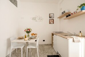 Una cocina compacta con una mesa de comedor para dos personas, una pequeña isla con fregadero y un estante montado en la pared con utensilios de cocina.