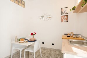 Cozinha compacta com área de refeições, apresentando uma mesa branca, cadeiras, bancada pequena e pia.