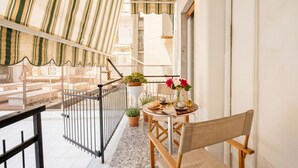 A balcony with a striped awning, a small table with chairs, potted plants, and a railing.