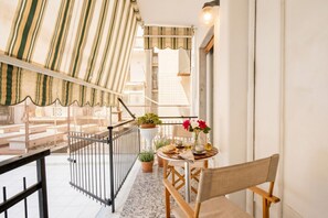 A balcony with a striped awning, a small table with chairs, potted plants, and a railing.