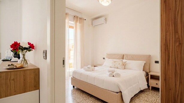 A bedroom with a bed, bedside tables, a nightstand, a wooden dresser, and a vase with flowers.
